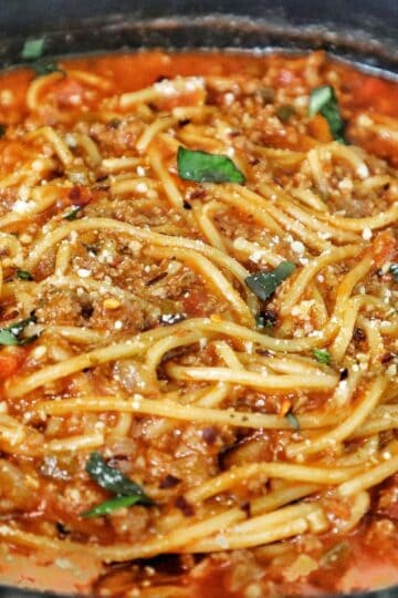 One pot spaghetti made with spaghetti noodles, ground beef, tomato sauce, and melted cheese, topped with fresh herbs.