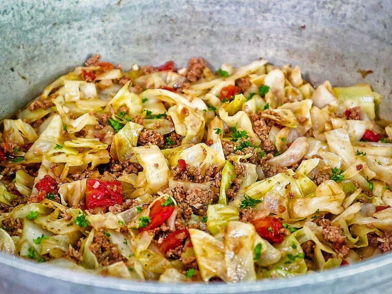 A skillet filled with sautéed cabbage, ground beef, diced tomatoes, and herbs, cooked to perfection in a large pot.