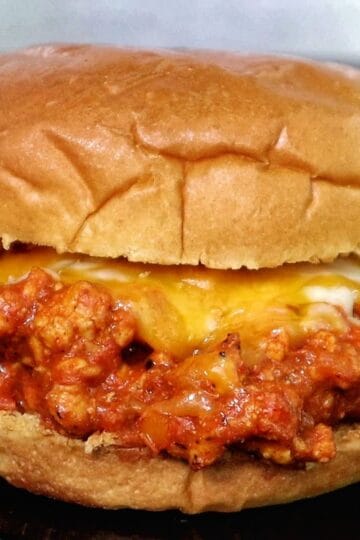 A Cajun Chicken Sloppy Joe served on a toasted hamburger bun, filled with a savory mix of ground chicken in a rich tomato-based Cajun sauce, topped with melted cheddar and mozzarella cheese.