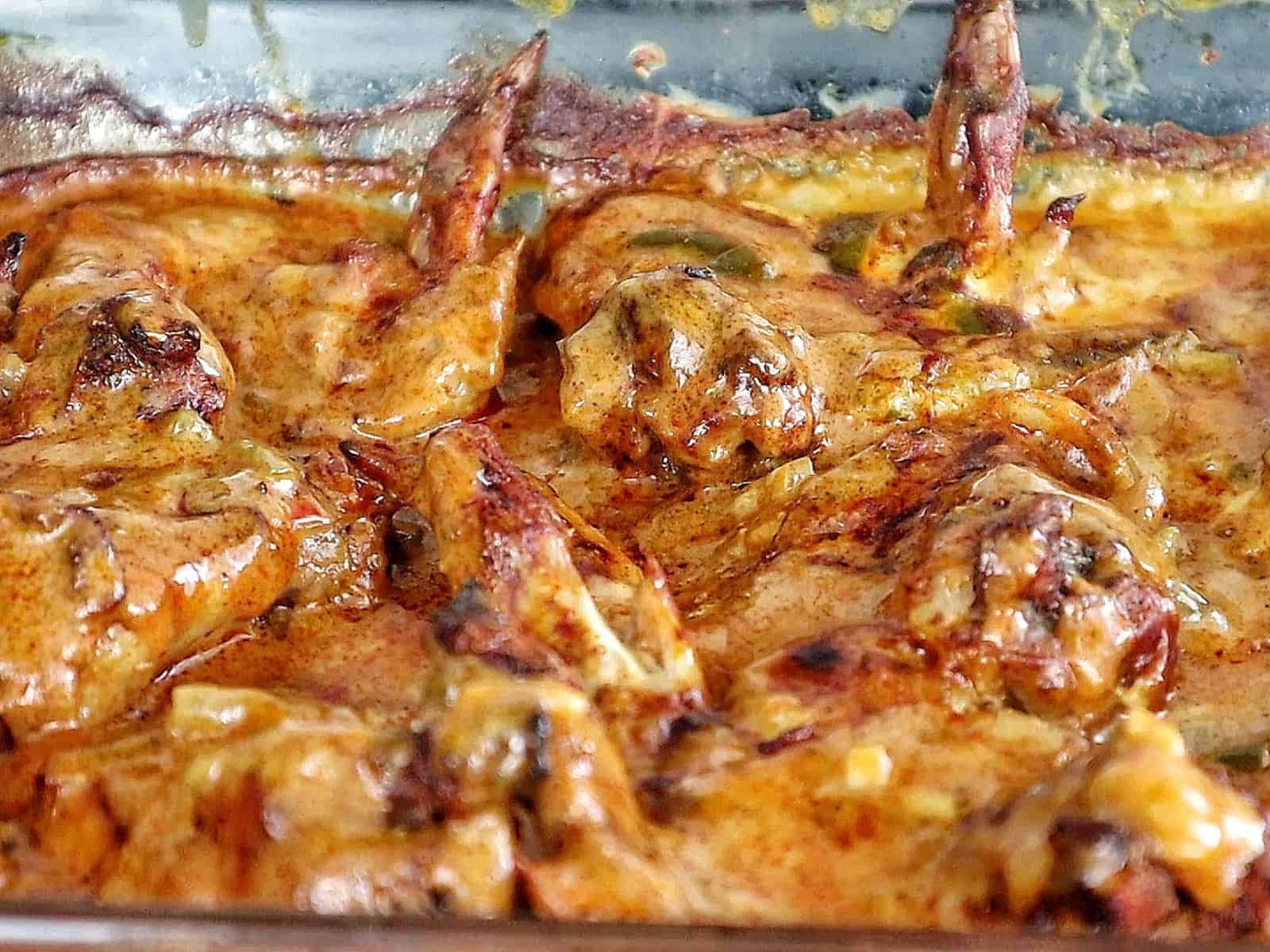 Close-up of juicy Cajun smothered chicken wings baked in a rich, creamy, golden-brown sauce with bits of peppers and onions.
