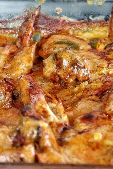 Close-up of juicy Cajun smothered chicken wings baked in a rich, creamy, golden-brown sauce with bits of peppers and onions.