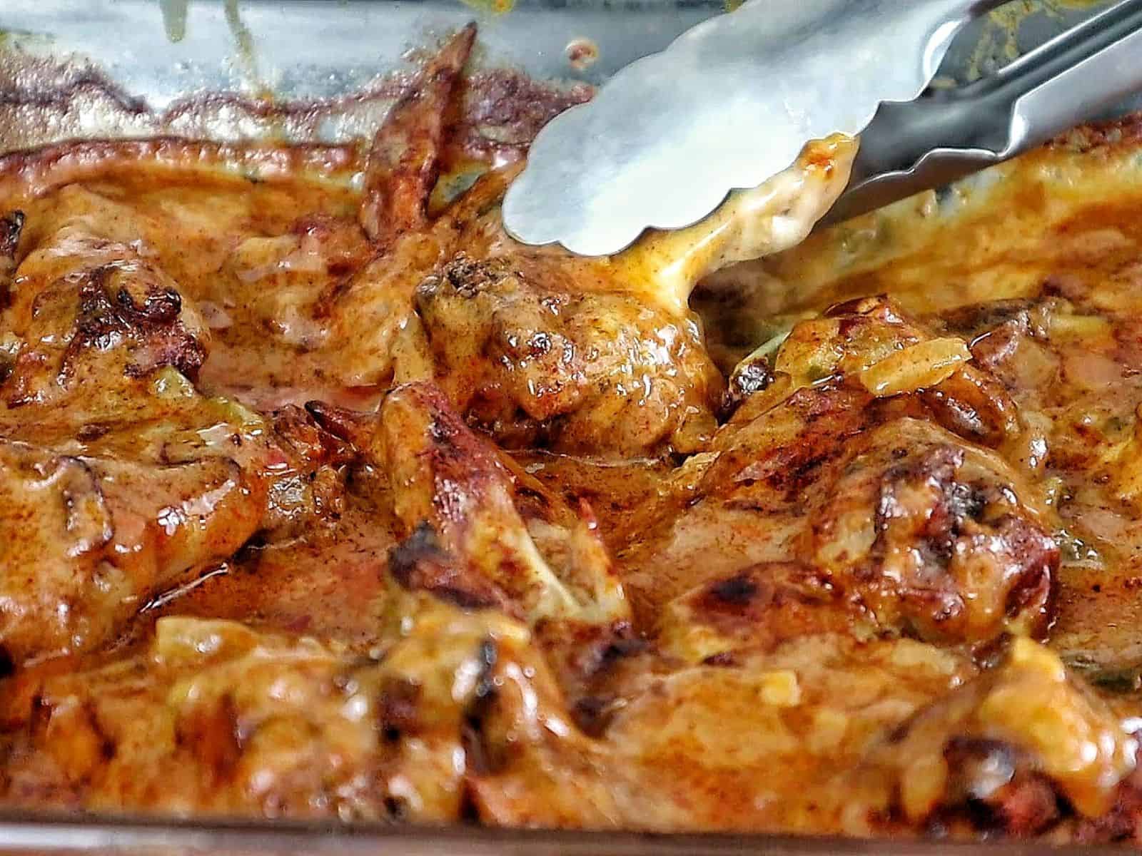 Close-up of juicy Cajun smothered chicken wings baked in a rich, creamy, golden-brown sauce with bits of peppers and onions.