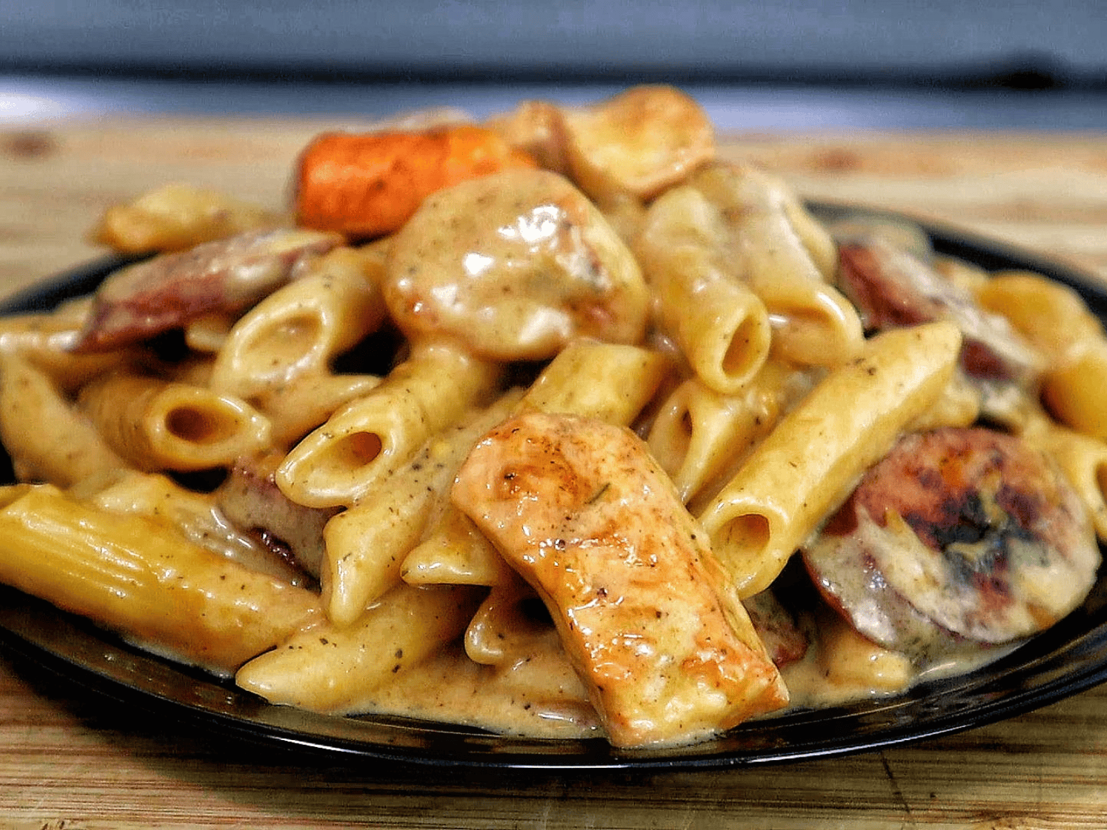 A creamy serving of cheesy ranch chicken and sausage pasta on a black plate. The dish features tender penne pasta coated in a ranch-seasoned cheese sauce, with seared chicken chunks and slices of smoked sausage.