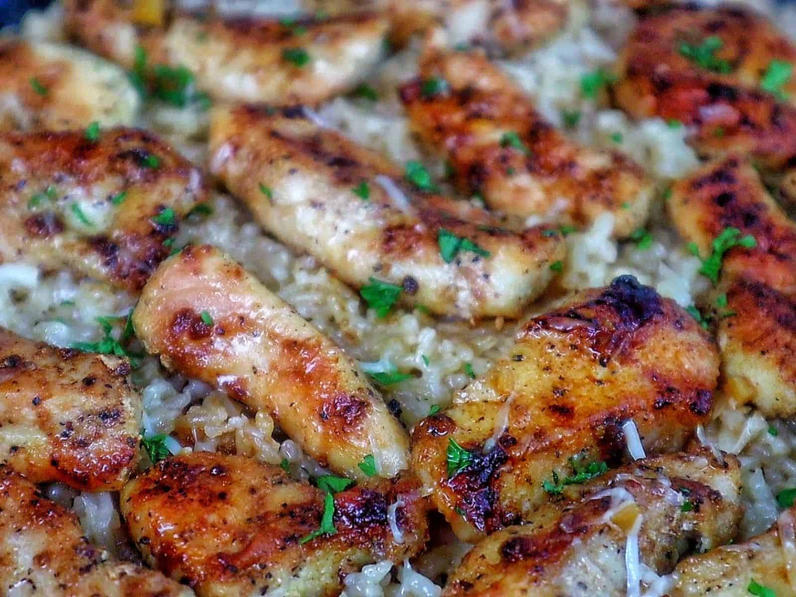 Golden brown seasoned chicken tenders on a bed of creamy garlic Parmesan rice, garnished with fresh parsley and parmesan cheese.

