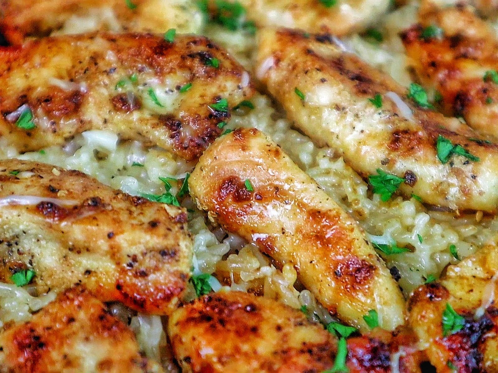 Golden brown seasoned chicken tenders on a bed of creamy garlic Parmesan rice, garnished with fresh parsley and parmesan cheese.