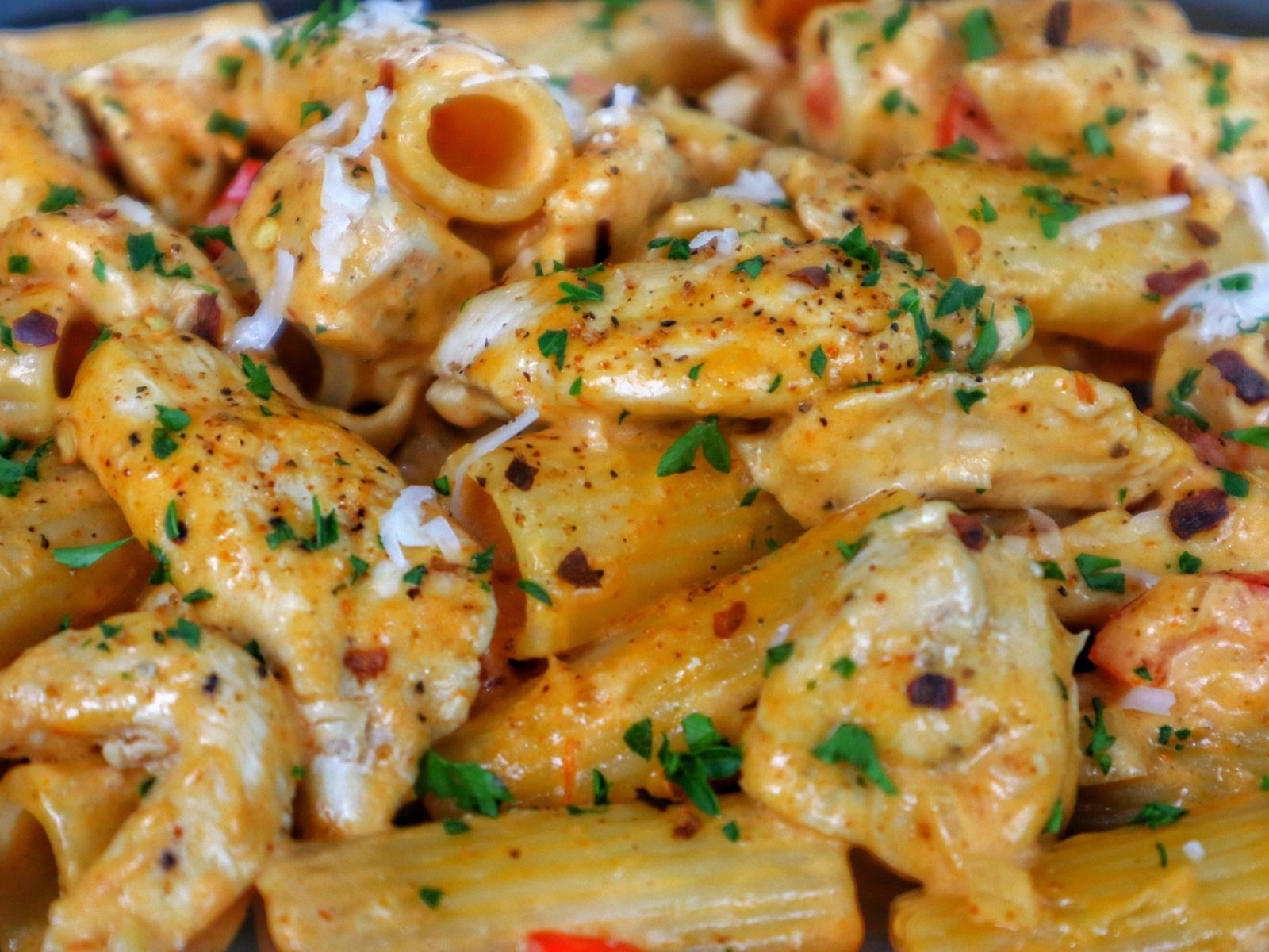 A plate of creamy Cajun chicken pasta made with rigatoni, tender chicken, red bell peppers, and a spicy Cajun cream sauce, garnished with chopped parsley and grated cheese.
