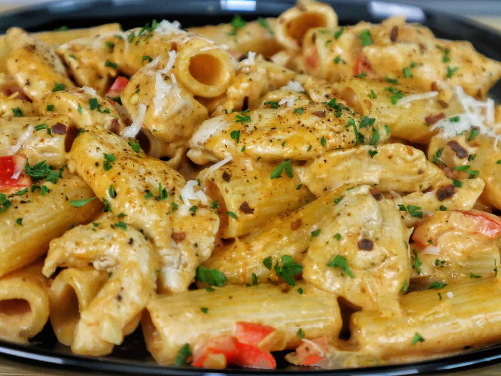 A plate of creamy Cajun chicken pasta made with rigatoni, tender chicken, red bell peppers, and a spicy Cajun cream sauce, garnished with chopped parsley and grated cheese.