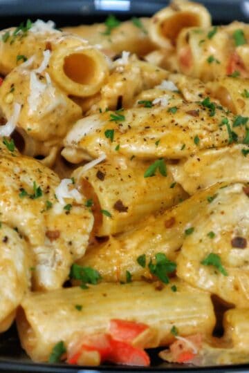 A plate of creamy Cajun chicken pasta made with rigatoni, tender chicken, red bell peppers, and a spicy Cajun cream sauce, garnished with chopped parsley and grated cheese.