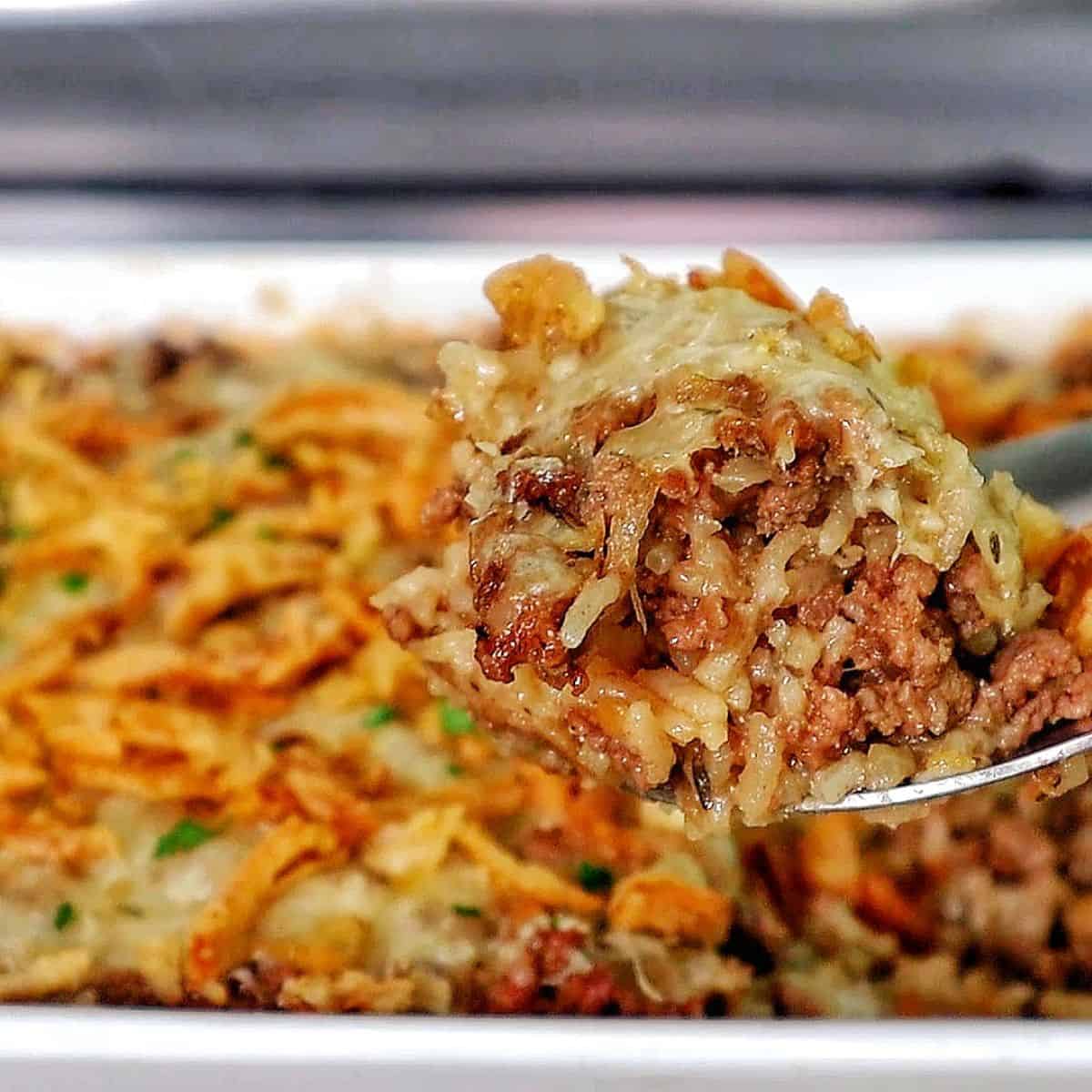 A close-up of a spoonful of French Onion Ground Beef and Rice Casserole, featuring tender ground beef, cooked rice, melted Swiss cheese, and crispy fried onions. 