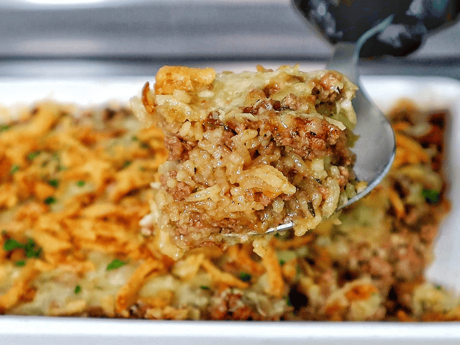 A close-up of a spoonful of French Onion Ground Beef and Rice Casserole, featuring tender ground beef, cooked rice, melted Swiss cheese, and crispy fried onions. 