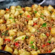 A cast iron skillet filled with a mixture of ground beef, tender potato chunks, red bell peppers, and chopped parsley, all simmered in a savory, seasoned sauce.