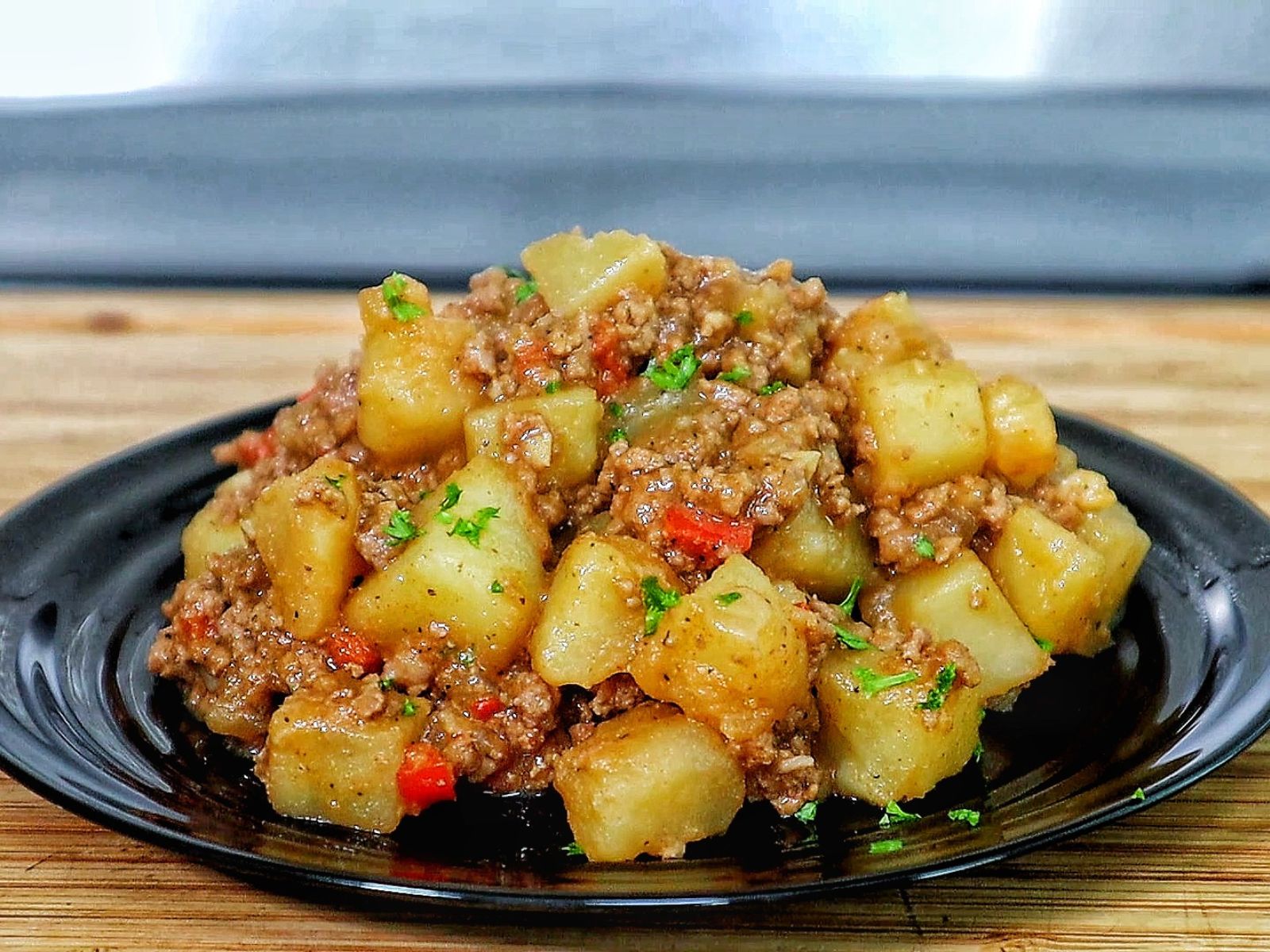 A cast iron skillet filled with a mixture of ground beef, tender potato chunks, red bell peppers, and chopped parsley, all simmered in a savory, seasoned sauce.