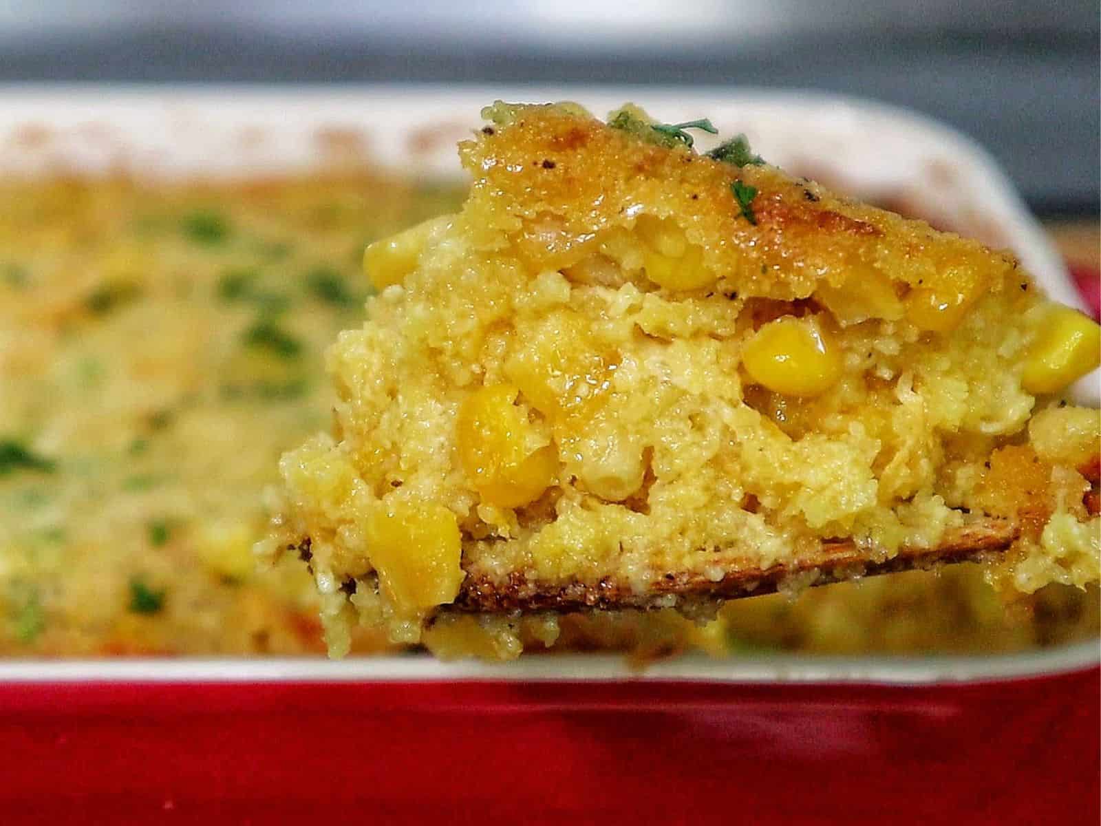 A close-up of a rich and golden honey glaze corn casserole being served from a baking dish. The texture looks soft, moist, and slightly crisp on top, with bits of corn visible throughout.