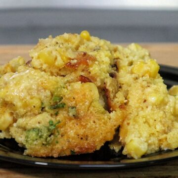 A close-up of a rich and golden honey glaze corn casserole being served from a baking dish. The texture looks soft, moist, and slightly crisp on top, with bits of corn visible throughout.