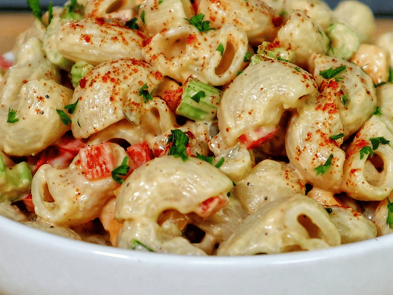 A creamy bowl of macaroni salad made with elbow pasta garnished with a sprinkle of paprika and chopped parsley.