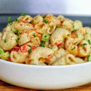 A creamy bowl of macaroni salad made with elbow pasta garnished with a sprinkle of paprika and chopped parsley.