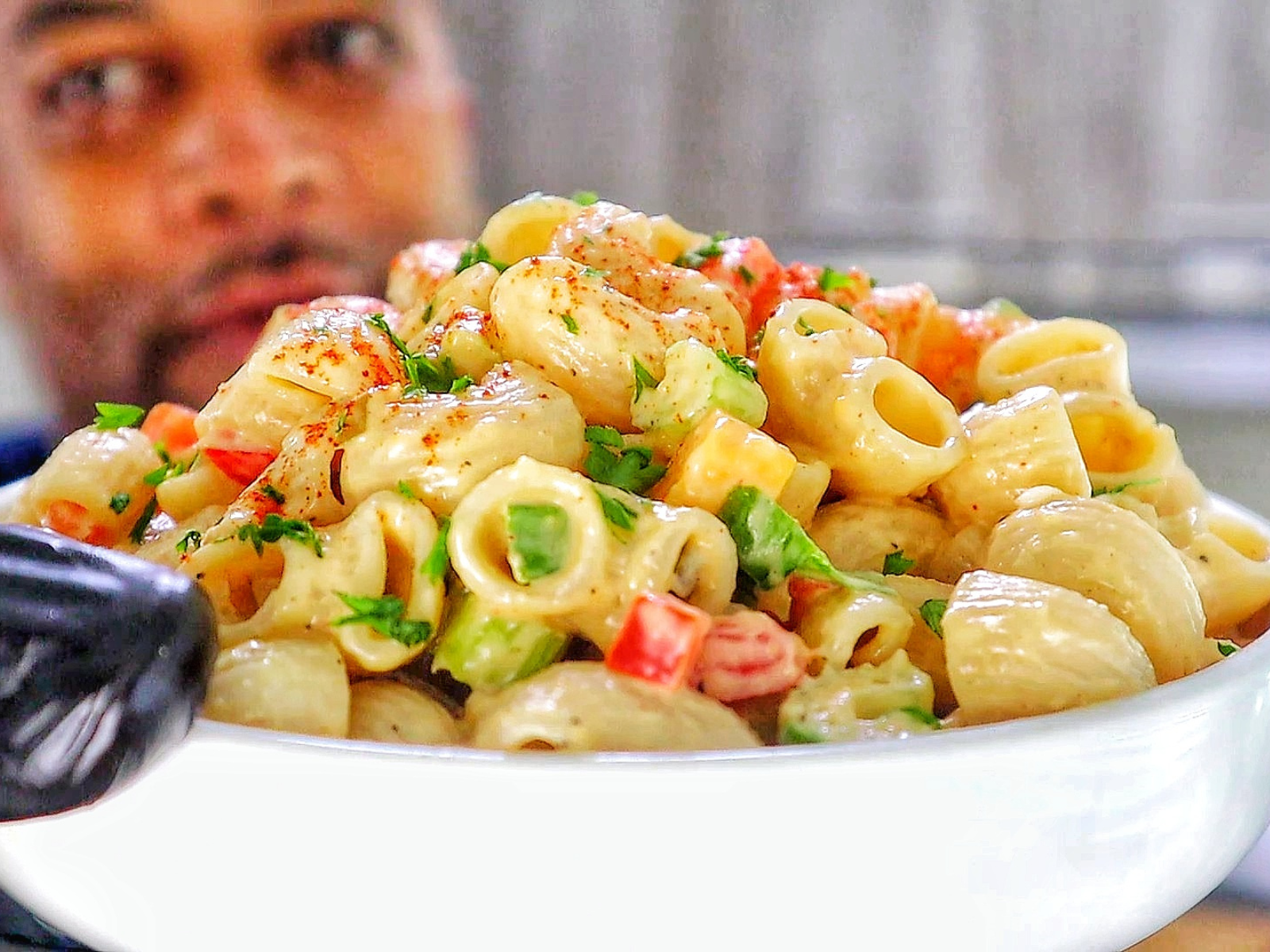 A creamy bowl of macaroni salad made with elbow pasta garnished with a sprinkle of paprika and chopped parsley.
