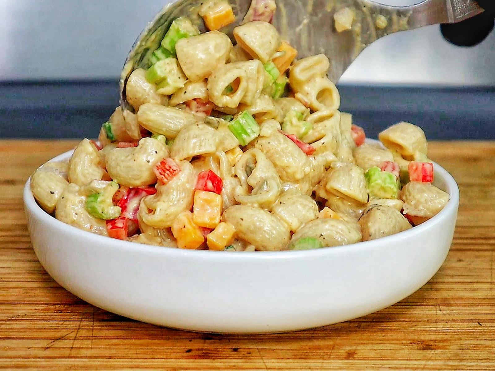 A creamy bowl of macaroni salad made with elbow pasta garnished with a sprinkle of paprika and chopped parsley.