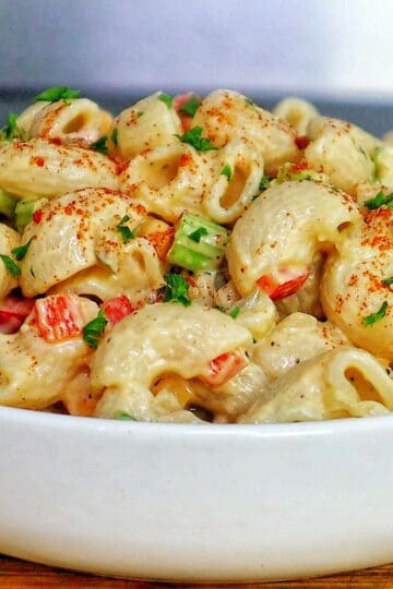 A creamy bowl of macaroni salad made with elbow pasta garnished with a sprinkle of paprika and chopped parsley.