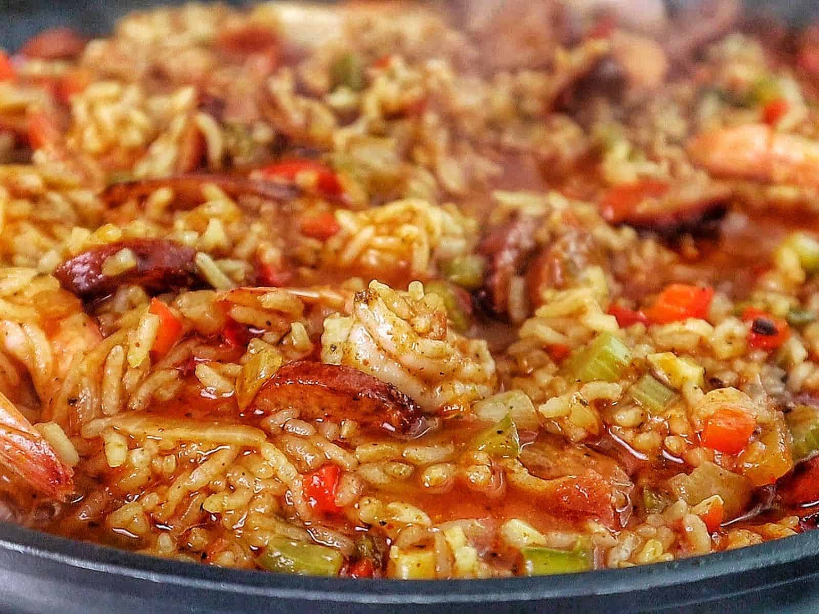 A pan filled with shrimp and sausage jambalaya, featuring juicy shrimp, sliced sausage, fluffy rice, and colorful diced vegetables garnished with fresh green onions.