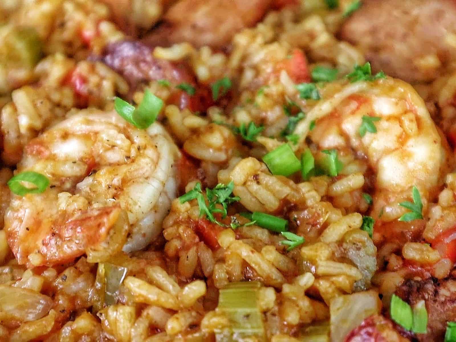 A pan filled with shrimp and sausage jambalaya, featuring juicy shrimp, sliced sausage, fluffy rice, and colorful diced vegetables garnished with fresh green onions.