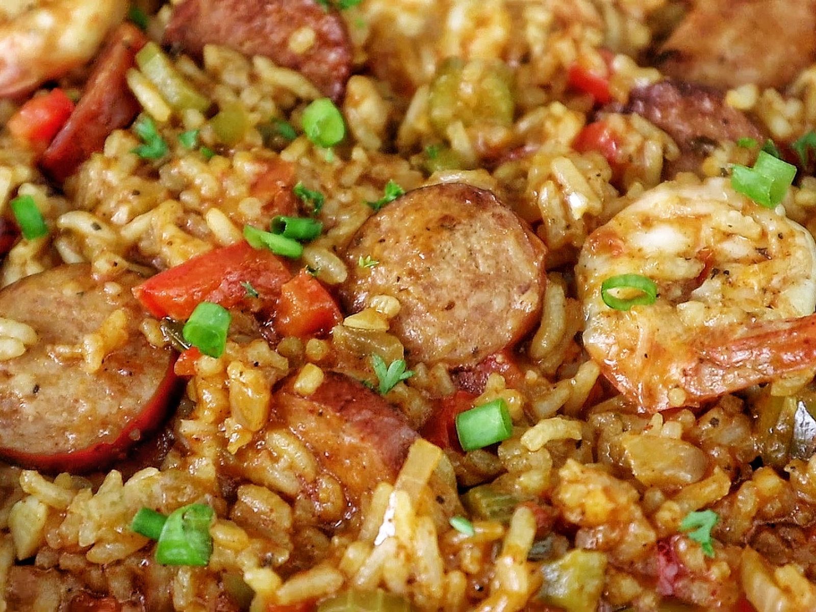 A pan filled with shrimp and sausage jambalaya, featuring juicy shrimp, sliced sausage, fluffy rice, and colorful diced vegetables garnished with fresh green onions.