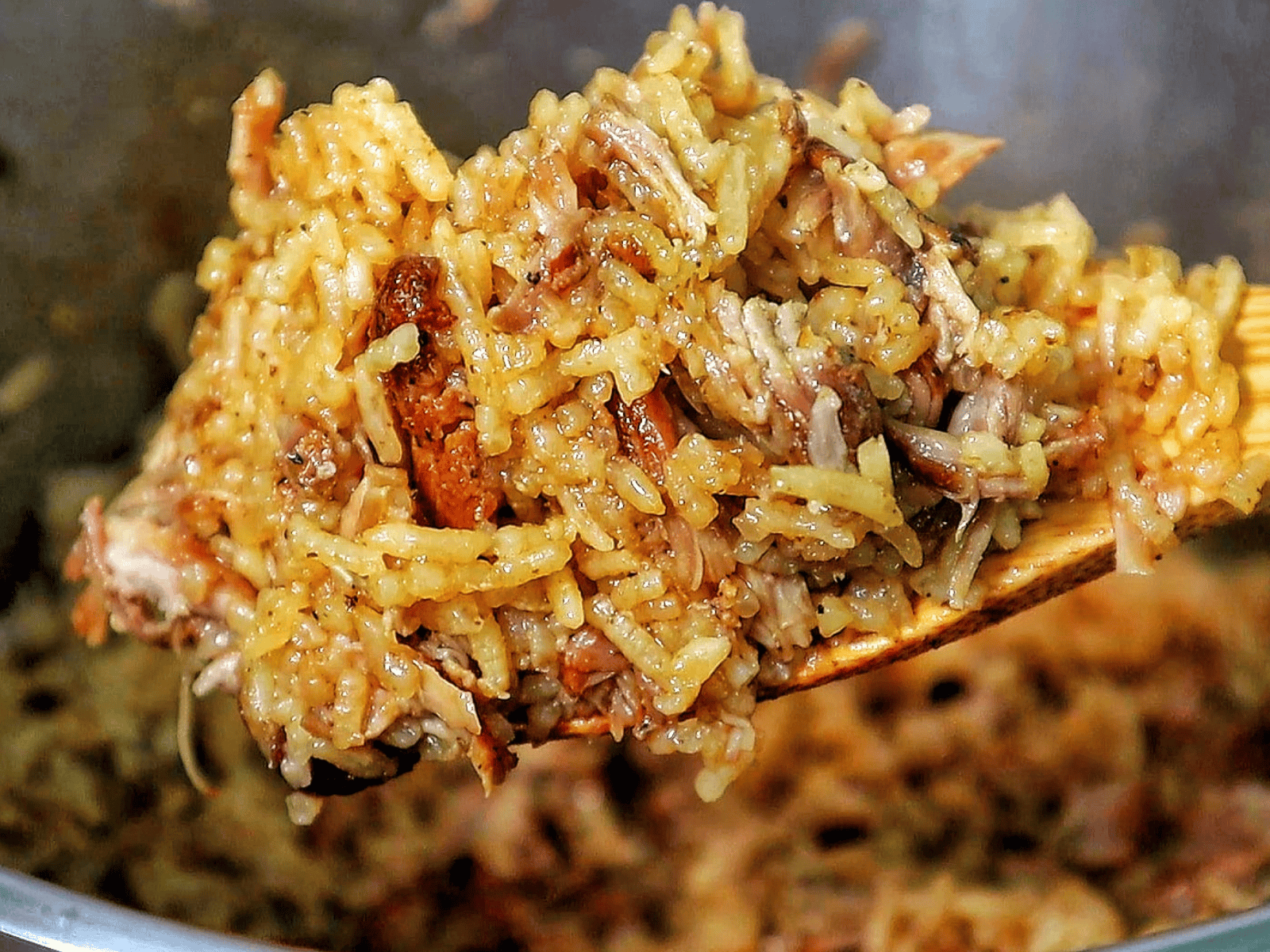 Close-up of a full serving of country-style ribs and rice, featuring tender, shredded rib meat mixed with seasoned, fluffy rice on a black plate.