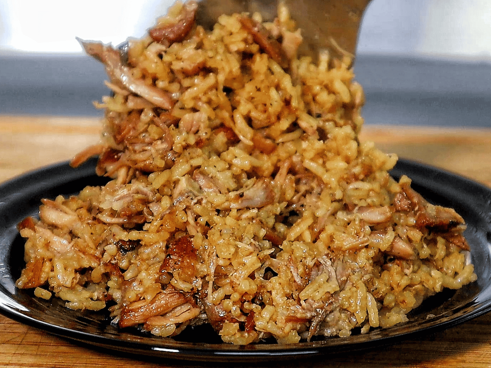Close-up of a full serving of country-style ribs and rice, featuring tender, shredded rib meat mixed with seasoned, fluffy rice on a black plate.