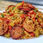 A healthy serving of rice and sausage skillet pasta on a white plate, featuring slices of browned sausage, tender rice, diced bell peppers, onions, and tomatoes., all mixed in a savory sauce and garnished with fresh chopped parsley.