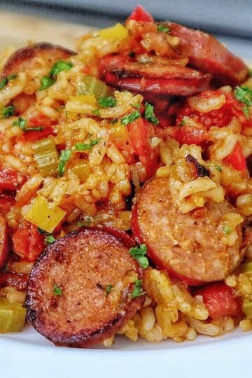 A healthy serving of rice and sausage skillet pasta on a white plate, featuring slices of browned sausage, tender rice, diced bell peppers, onions, and tomatoes., all mixed in a savory sauce and garnished with fresh chopped parsley.