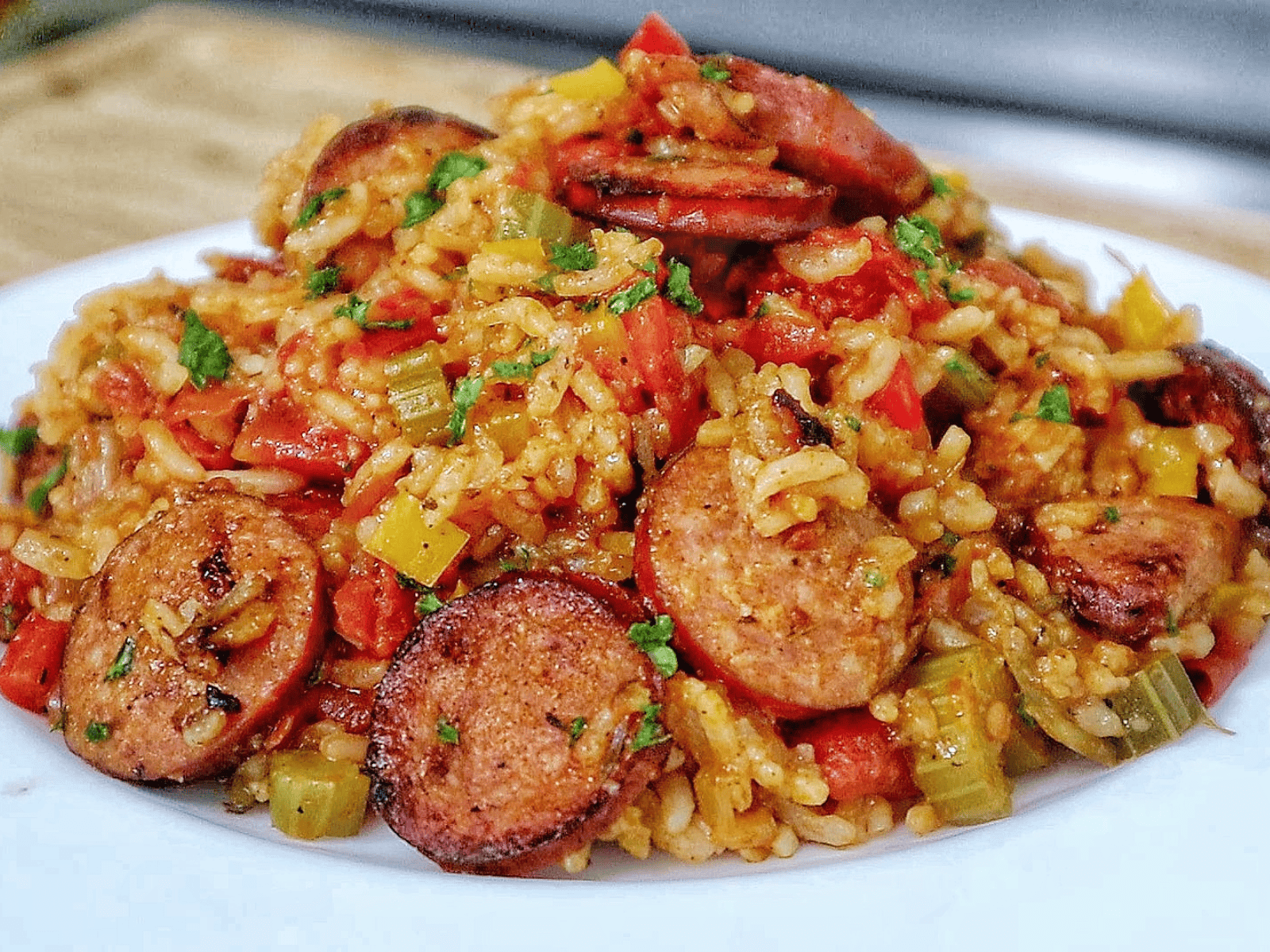 A healthy serving of rice and sausage skillet pasta on a white plate, featuring slices of browned sausage, tender rice, diced bell peppers, onions, and tomatoes., all mixed in a savory sauce and garnished with fresh chopped parsley.