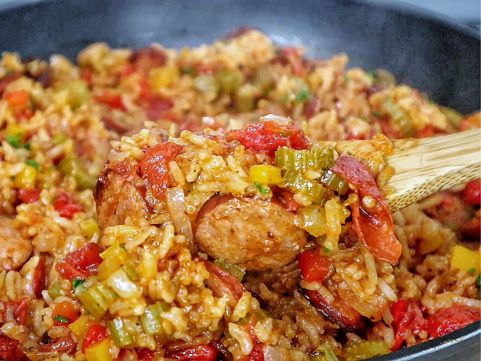 A healthy serving of rice and sausage skillet pasta on a white plate, featuring slices of browned sausage, tender rice, diced bell peppers, onions, and tomatoes., all mixed in a savory sauce and garnished with fresh chopped parsley.