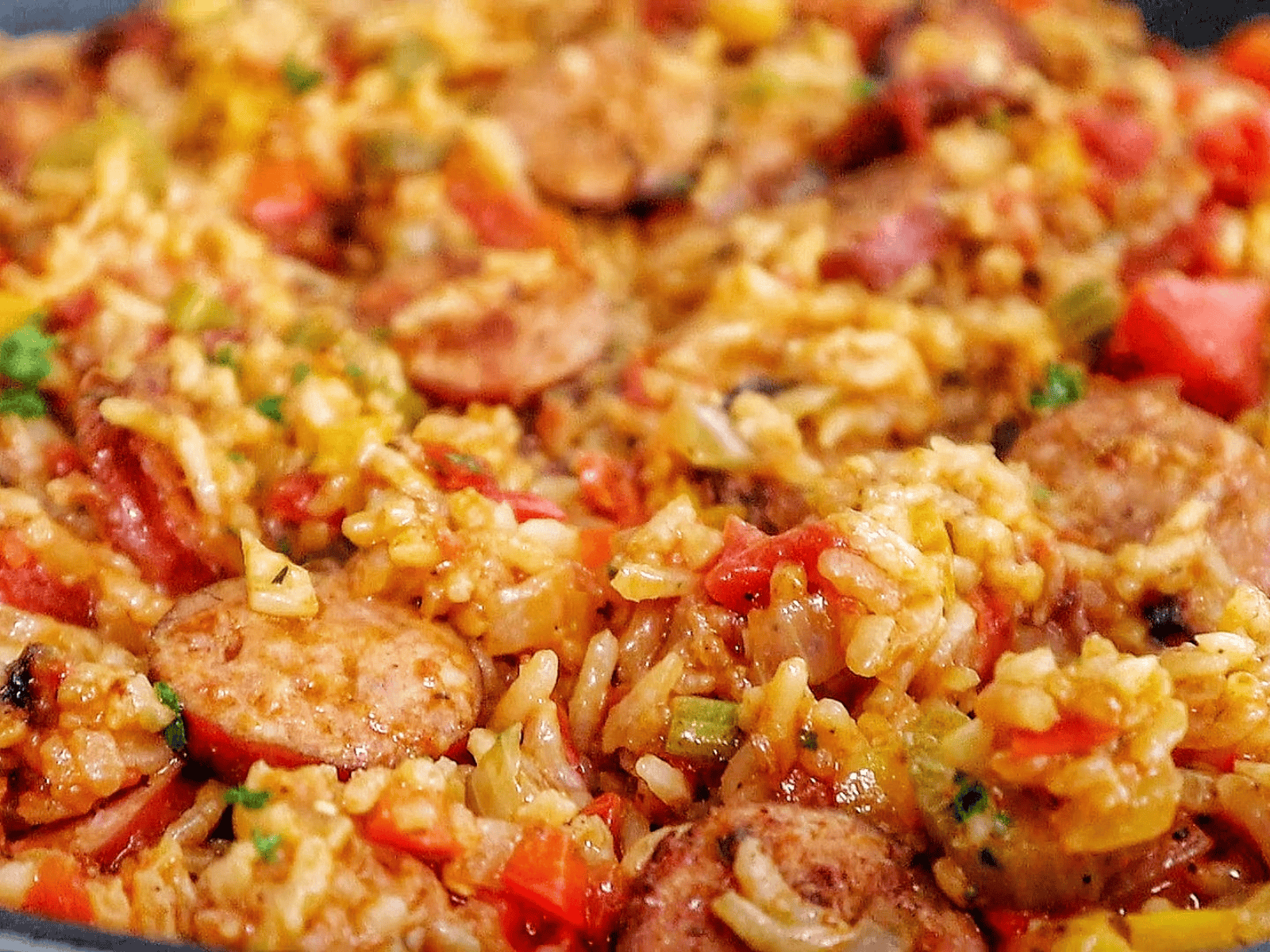 A healthy serving of rice and sausage skillet pasta on a white plate, featuring slices of browned sausage, tender rice, diced bell peppers, onions, and tomatoes., all mixed in a savory sauce and garnished with fresh chopped parsley.