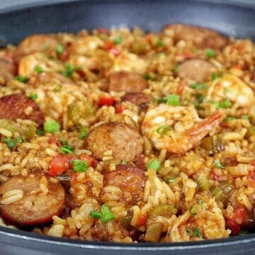 A pan filled with shrimp and sausage jambalaya, featuring juicy shrimp, sliced sausage, fluffy rice, and colorful diced vegetables garnished with fresh green onions.