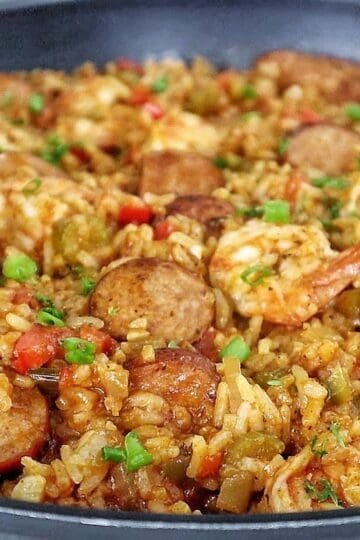 A pan filled with shrimp and sausage jambalaya, featuring juicy shrimp, sliced sausage, fluffy rice, and colorful diced vegetables garnished with fresh green onions.