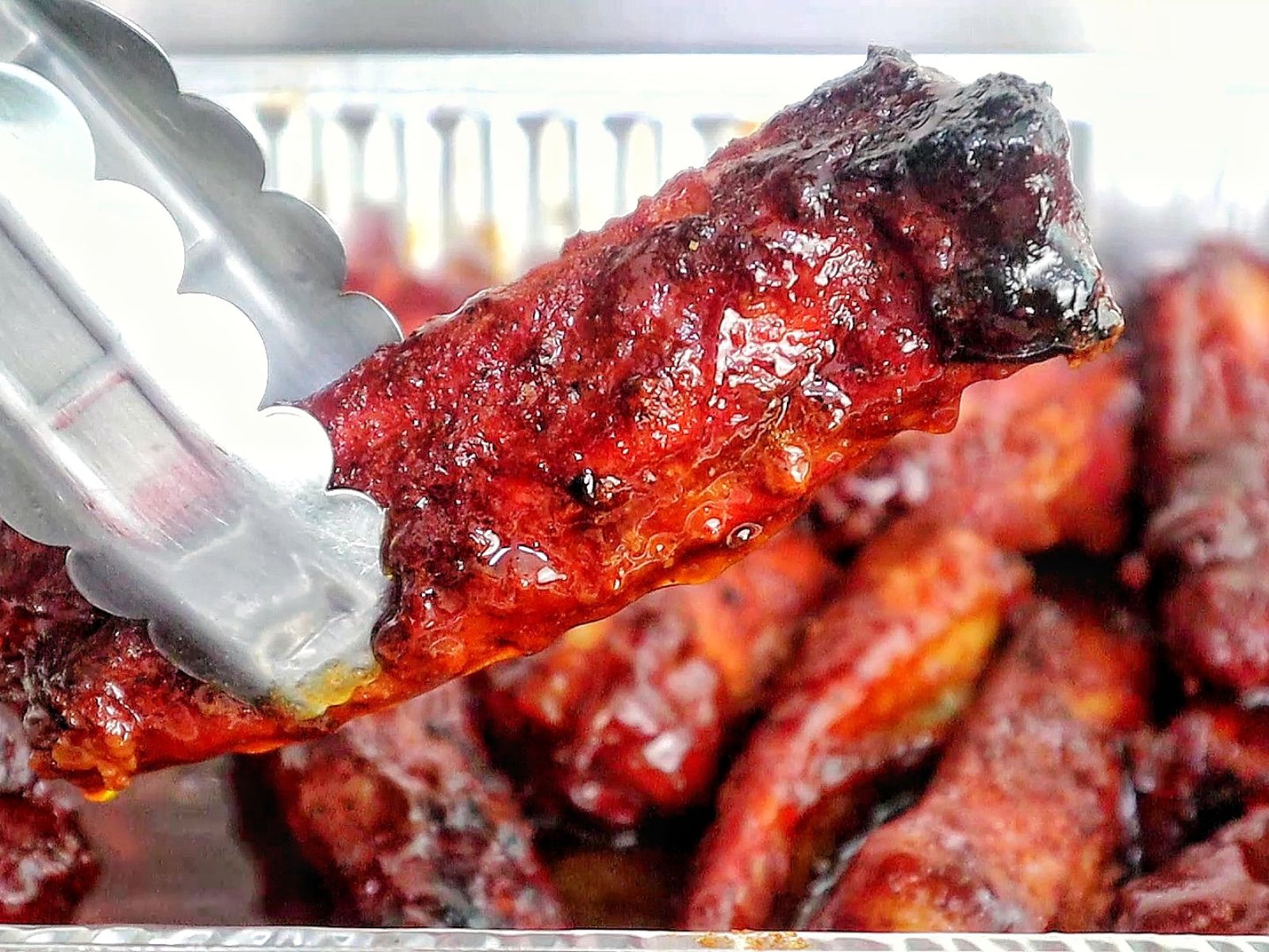 A close-up of juicy smoked BBQ ribs fresh off a pellet grill. The ribs are coated in a barbecue sauce with a deep caramelized glaze and visible char marks, highlighting their smoky, tender texture.