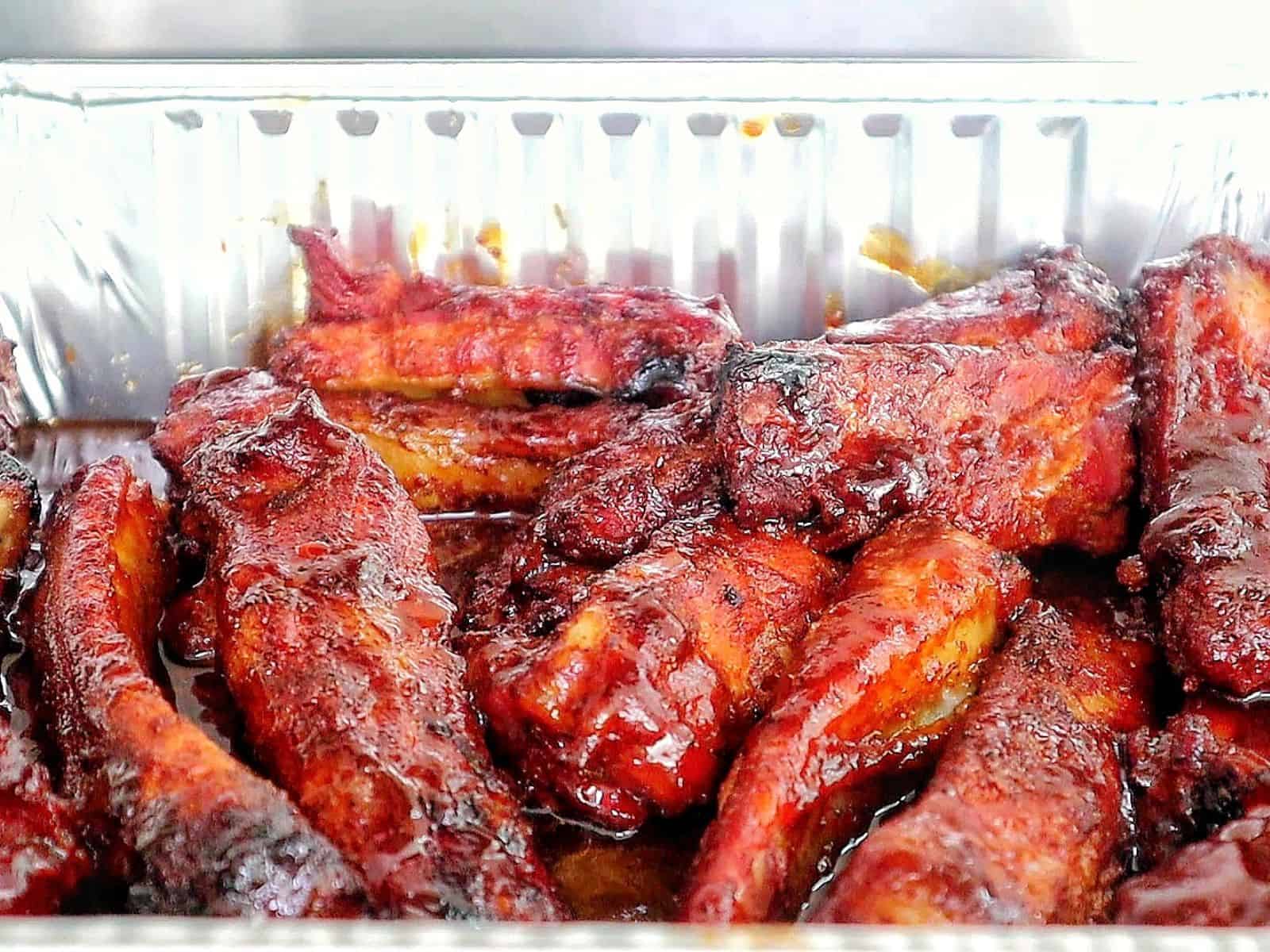 A close-up of juicy smoked BBQ ribs fresh off a pellet grill. The ribs are coated in a barbecue sauce with a deep caramelized glaze and visible char marks, highlighting their smoky, tender texture.