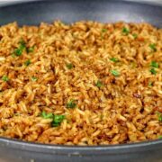 A close-up image of a skillet filled with golden-brown, seasoned rice garnished with fresh parsley, resembling the original recipe for Texas Roadhouse seasoned rice side dish.