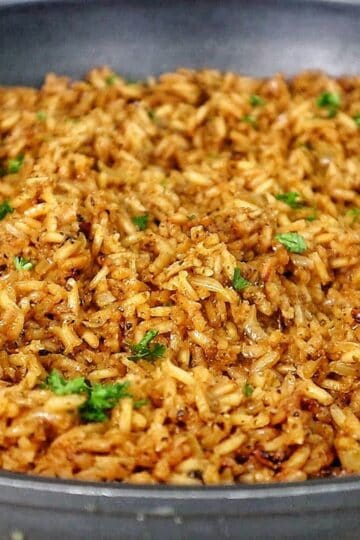 A close-up image of a skillet filled with golden-brown, seasoned rice garnished with fresh parsley, resembling the original recipe for Texas Roadhouse seasoned rice side dish.