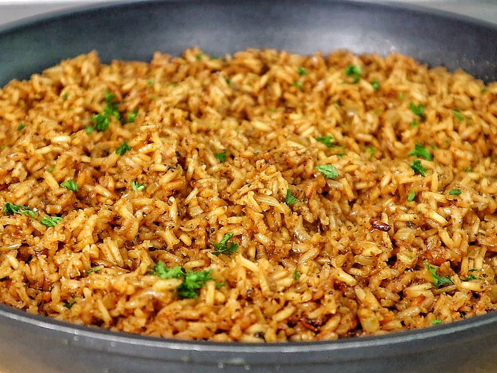 A close-up image of a skillet filled with golden-brown, seasoned rice garnished with fresh parsley, resembling the original recipe for Texas Roadhouse seasoned rice side dish.