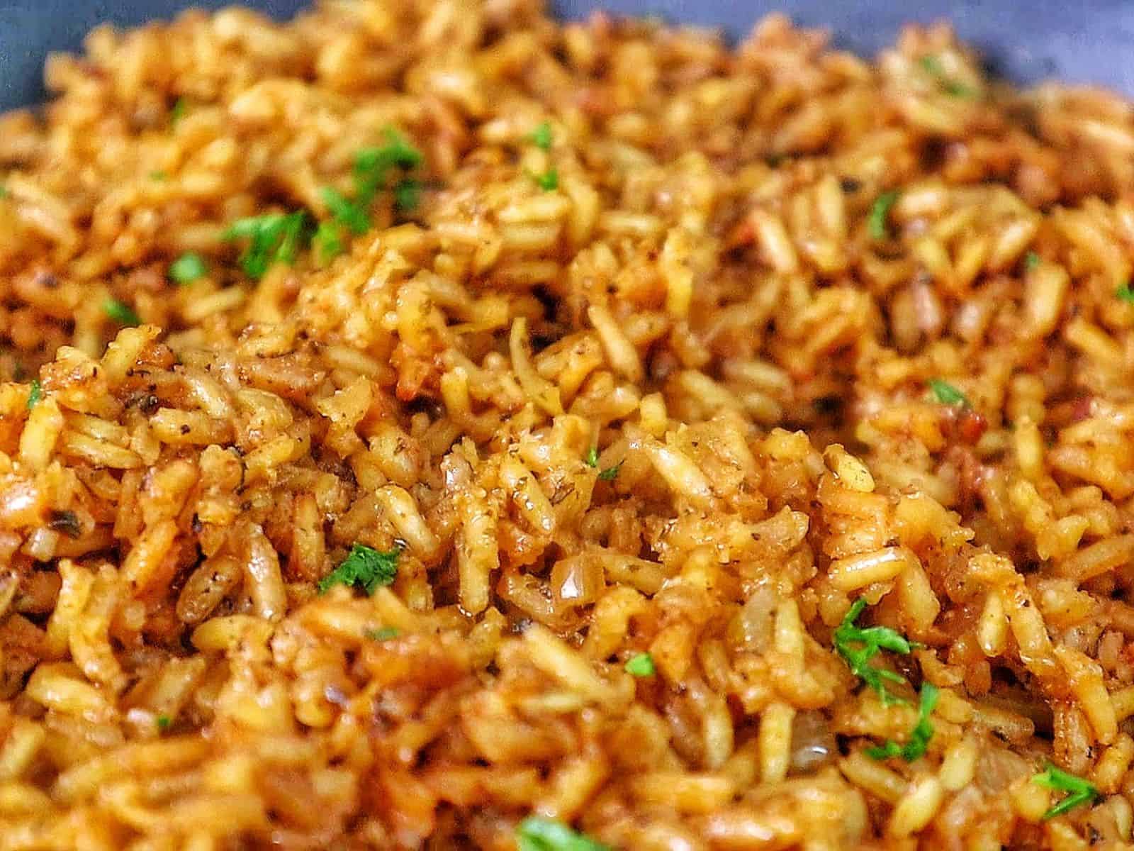 A close-up image of a skillet filled with golden-brown, seasoned rice garnished with fresh parsley, resembling the original recipe for Texas Roadhouse seasoned rice side dish.