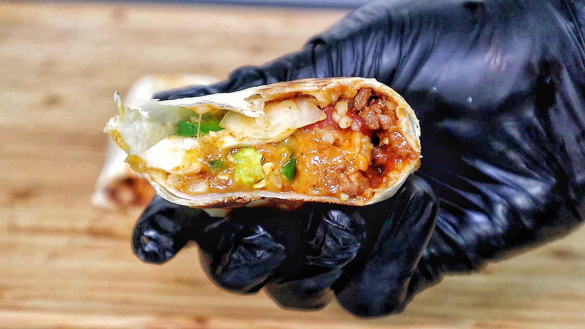 A stack of grilled chili cheese burritos, stuffed with seasoned ground beef, melted cheese, rice, beans, and sliced jalapeños.