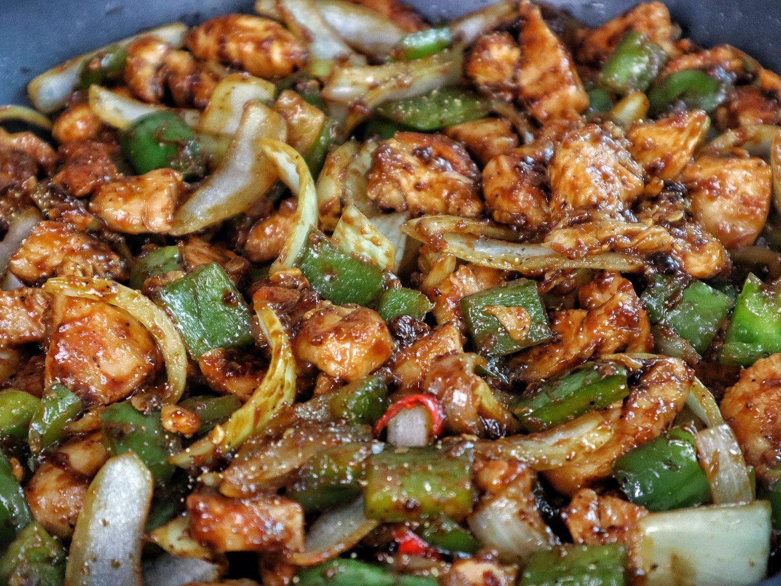 Sizzling black pepper chicken stir-fry with green bell peppers and onions coated in a rich black pepper sauce served in a skillet.