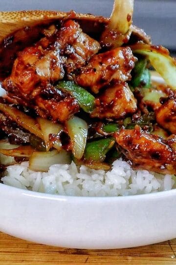 Sizzling black pepper chicken stir-fry with green bell peppers and onions coated in a rich, black pepper sauce served in a skillet.