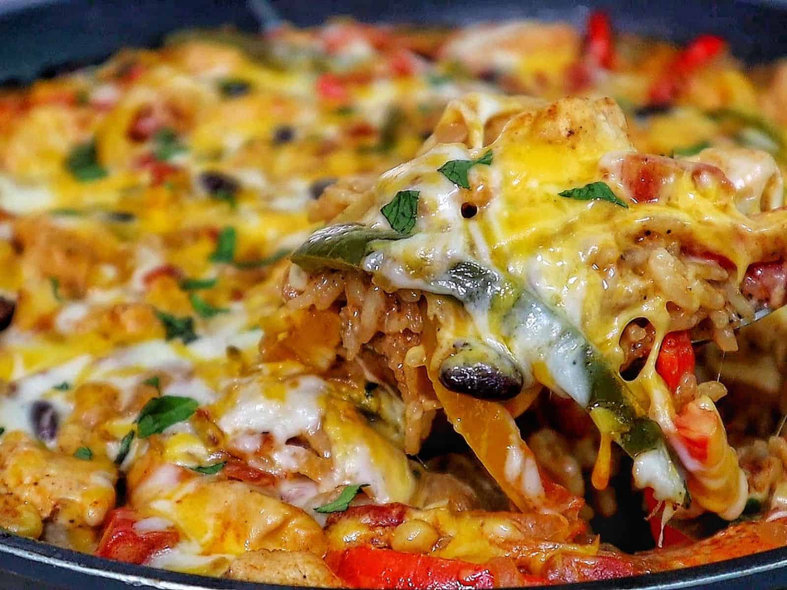 Cheesy chicken fajita rice casserole, showing bell peppers, melted cheese, and tender chicken scooped from a skillet.
