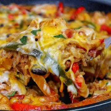 Cheesy chicken fajita rice casserole, showing bell peppers, melted cheese, and tender chicken scooped from a skillet.
