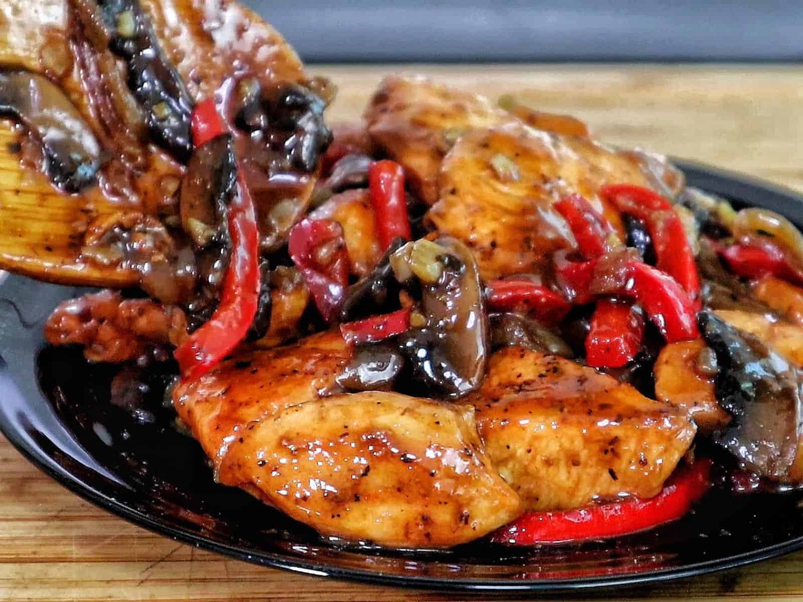 Black Pepper Chicken with Mushrooms served on a black plate, with seared chicken strips, sautéed red and green bell peppers, and mushrooms coated in a black pepper sauce.