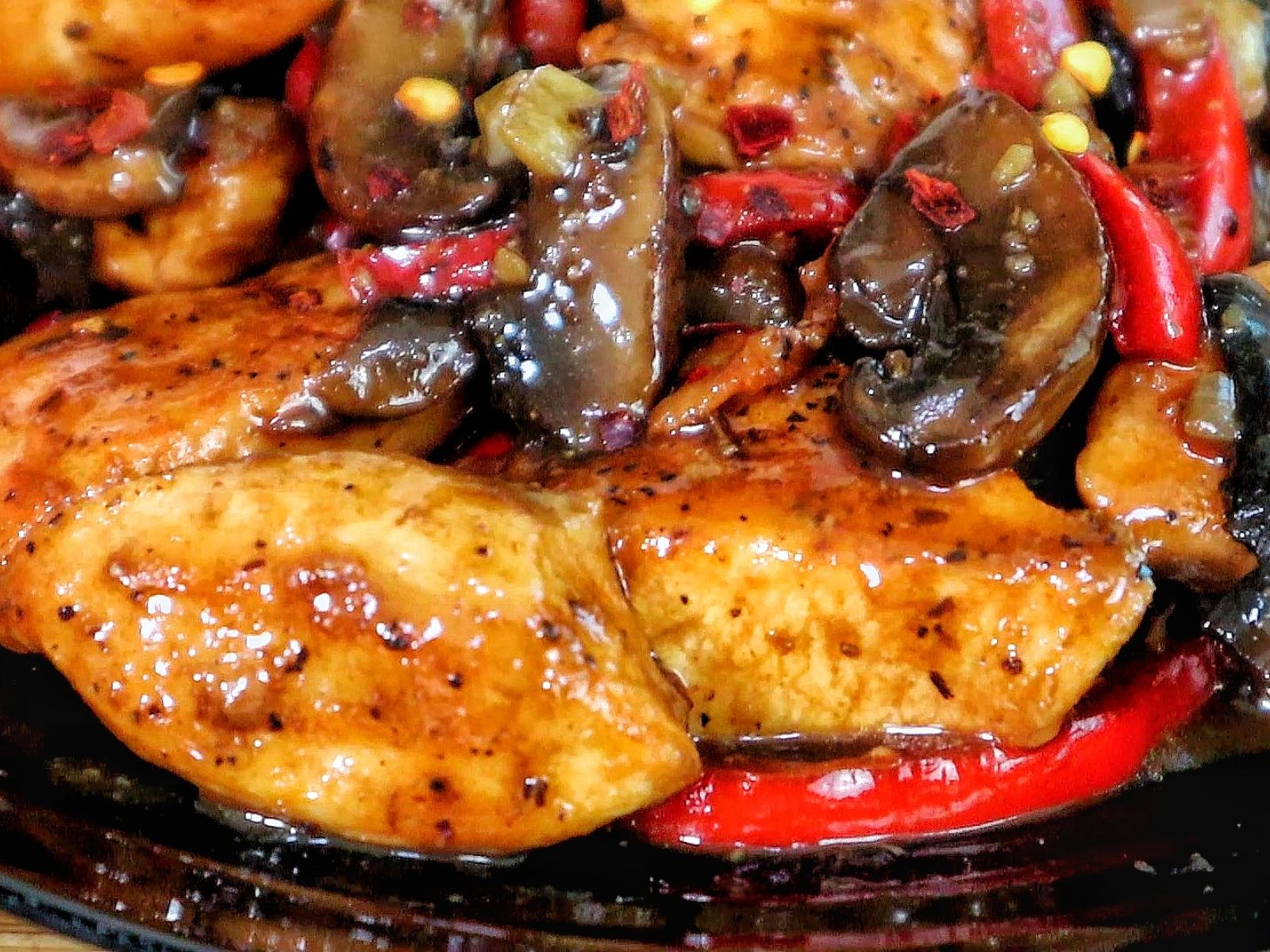 Black Pepper Chicken with Mushrooms served on a black plate, with seared chicken strips, sautéed red and green bell peppers, and mushrooms coated in a black pepper sauce.