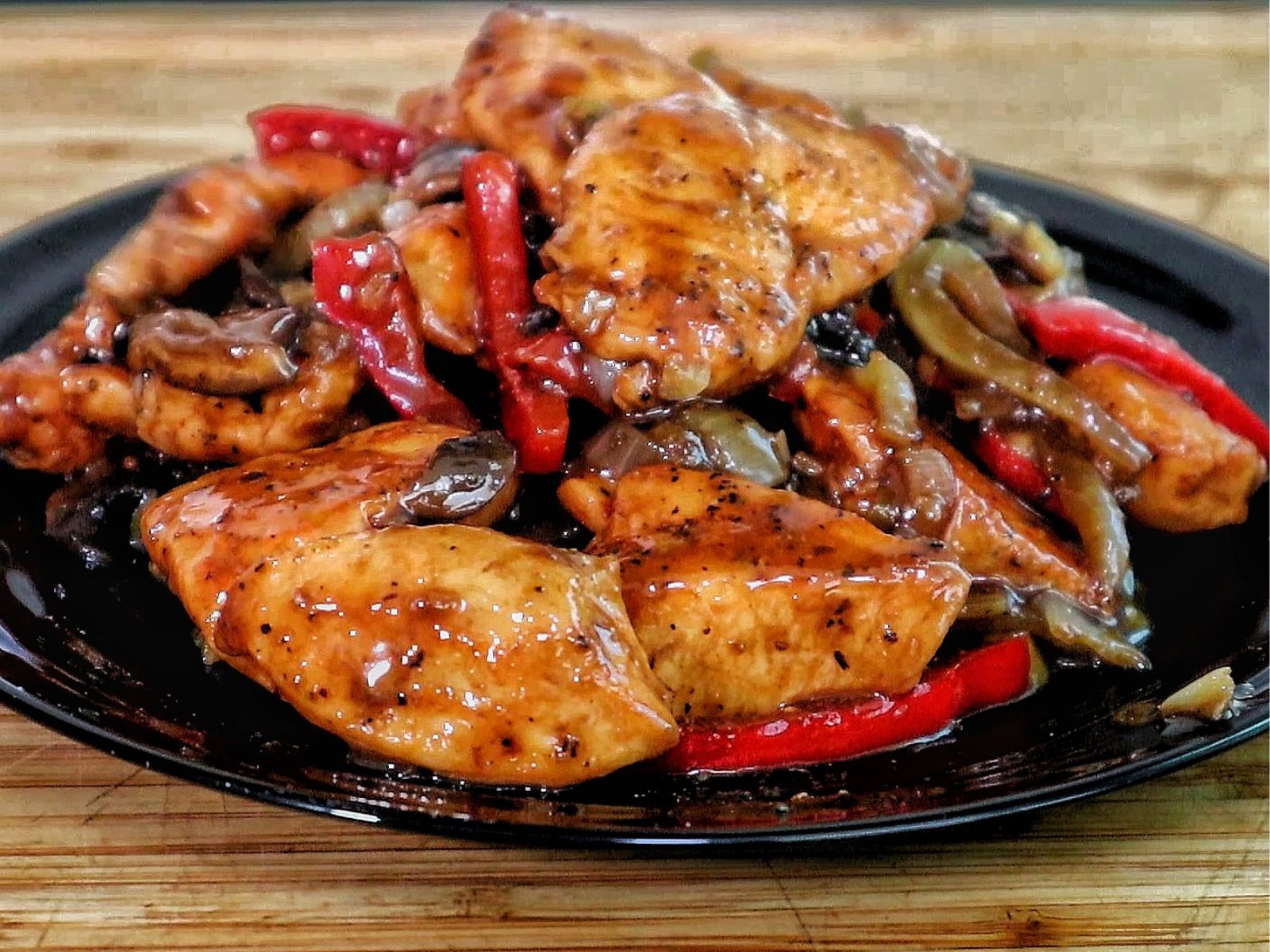 Black Pepper Chicken with Mushrooms served on a black plate, with seared chicken strips, sautéed red and green bell peppers, and mushrooms coated in a black pepper sauce.