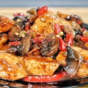 Black Pepper Chicken with Mushrooms served on a black plate, with seared chicken strips, sautéed red and green bell peppers, and mushrooms coated in a black pepper sauce.